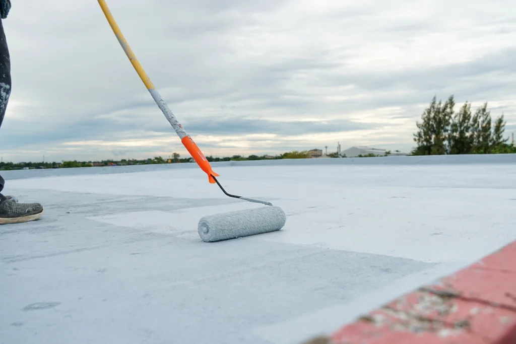 roller applying elastomeric roof coating onto a flat roof for a commercial property