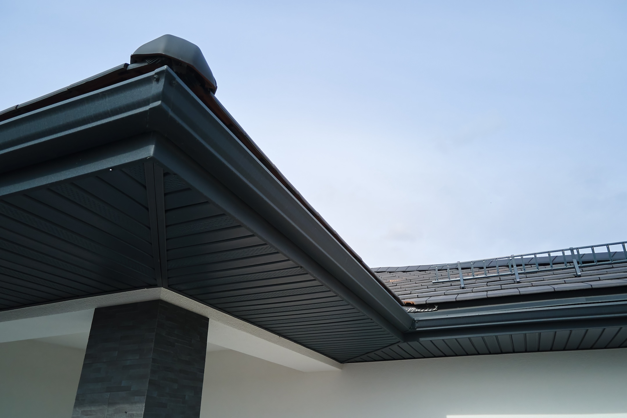 House corner with brown metal planks siding and roof with steel gutter rain system. Roofing, construction, drainage pipes installation.